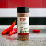 Uncle Clarence BBQ bold rib seasoning mix in a clear jar with red chili peppers in the background