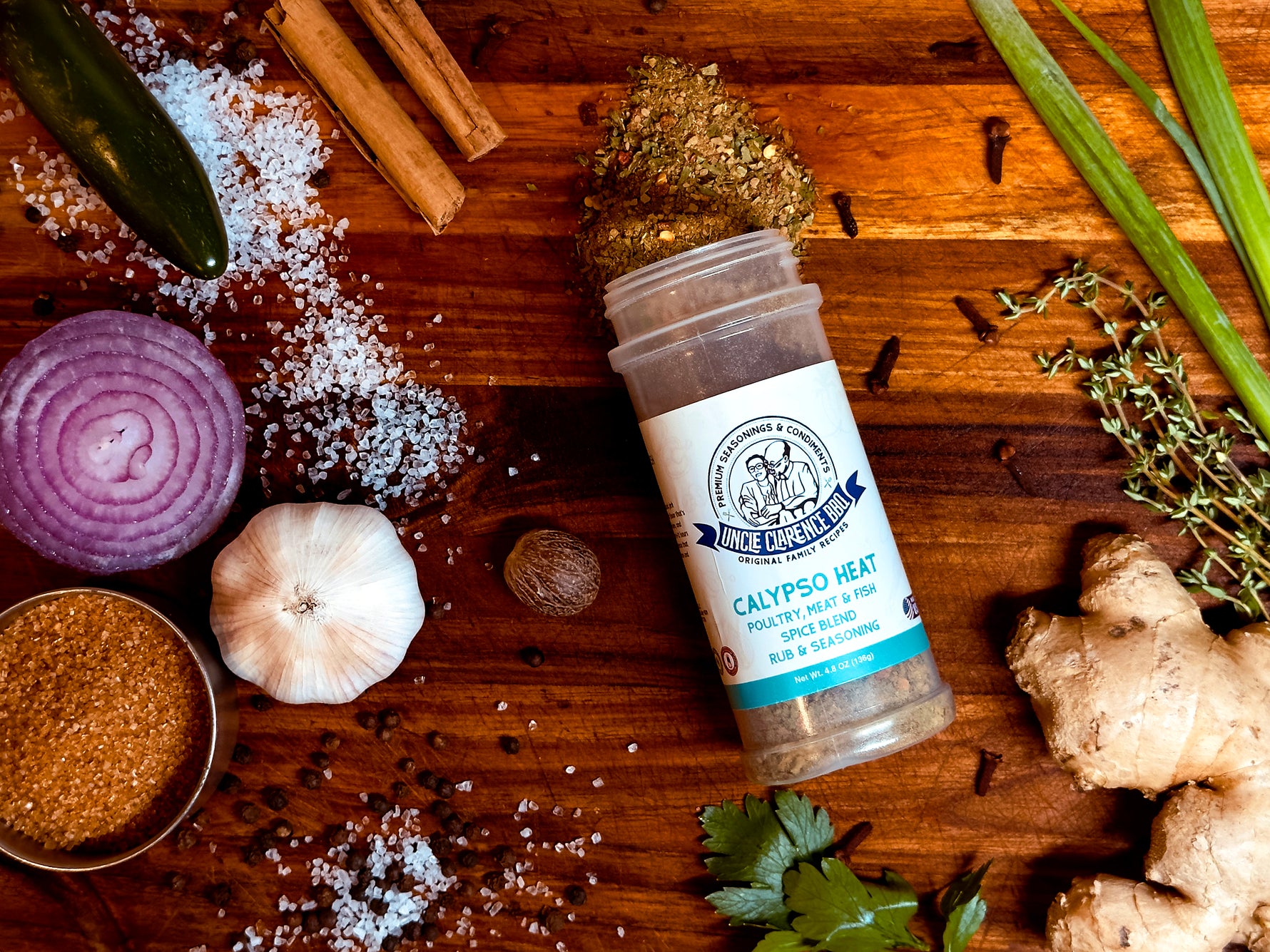 Uncle Clarence spice set featuring Calypso Heat seasoning with fresh herbs and vegetables on a wooden table